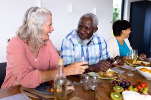 Happy multiracial senior friends talking while having lunch at dining table in nursing home