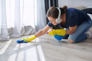 Home cleaning on positive, woman in headphones gloves cleans floor