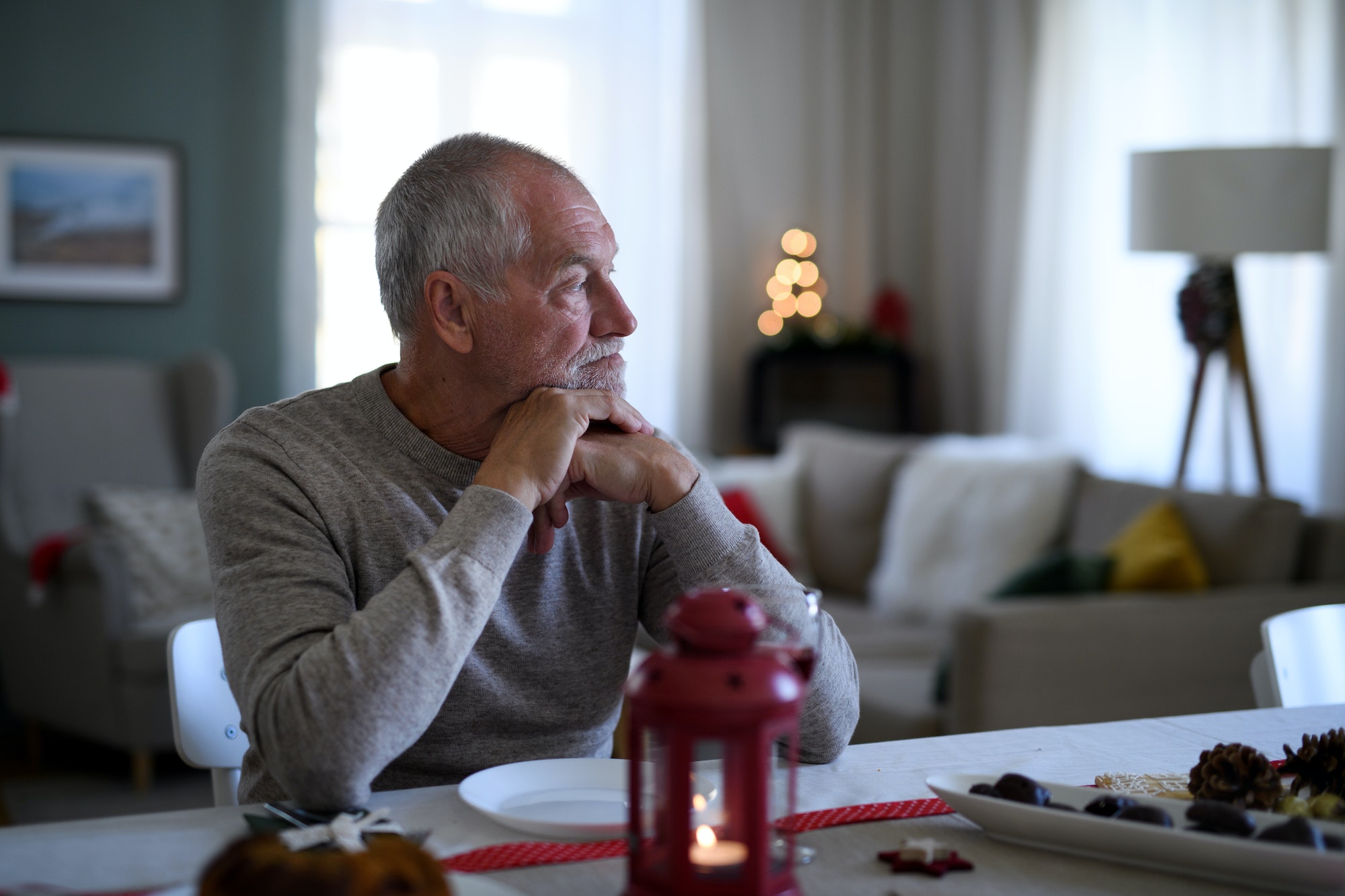 Lonely senior man sitting at the table indoors at Christmas, solitude concept