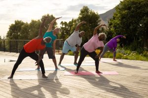 Multiracial seniors exercising on mats over hardwood floor against plants in yard