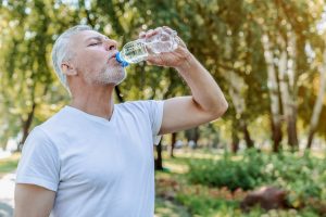 Senior man drinking water after workout in park.