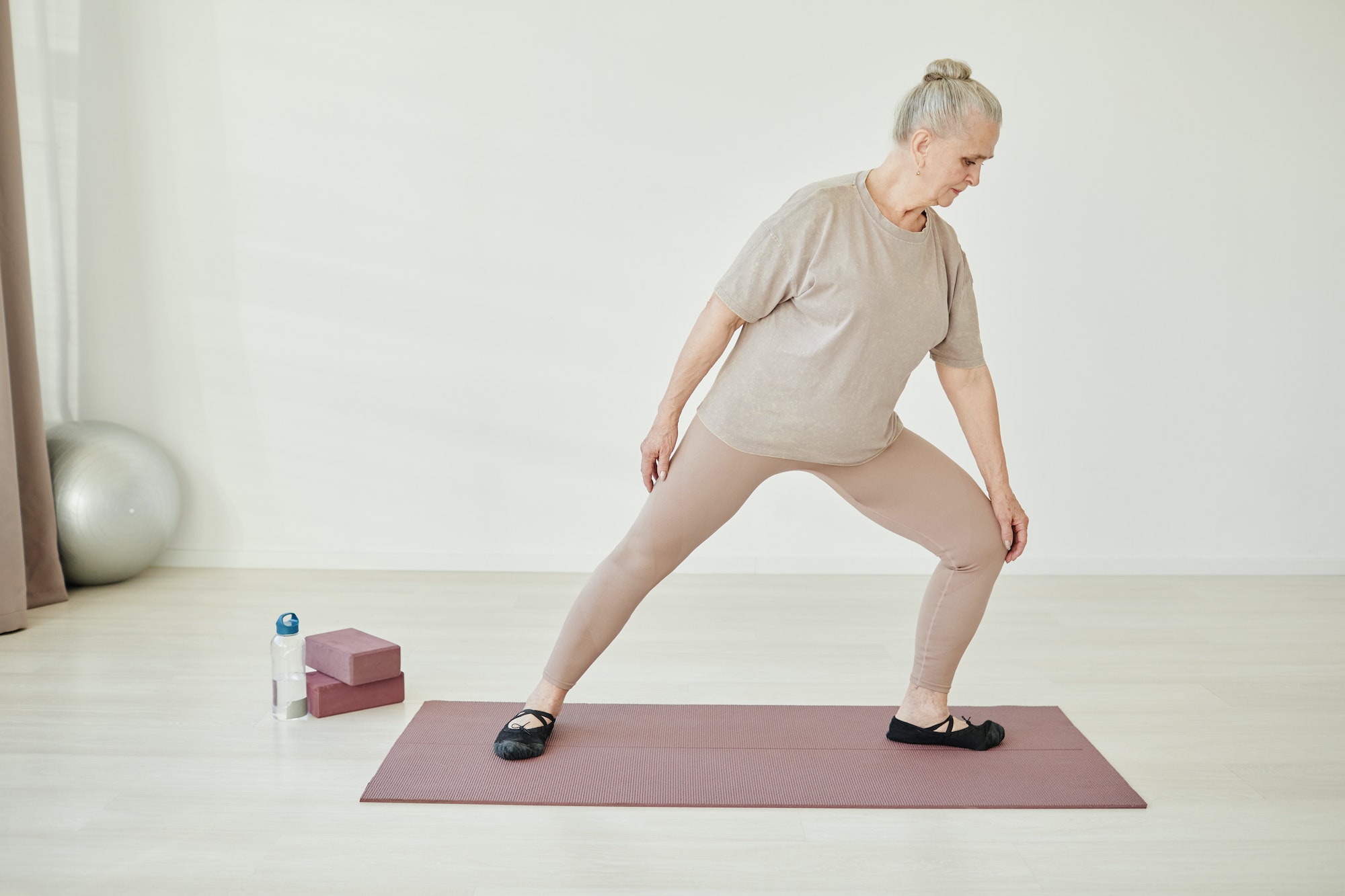 Senior woman in activewear keeping one leg bent in knee during exercise