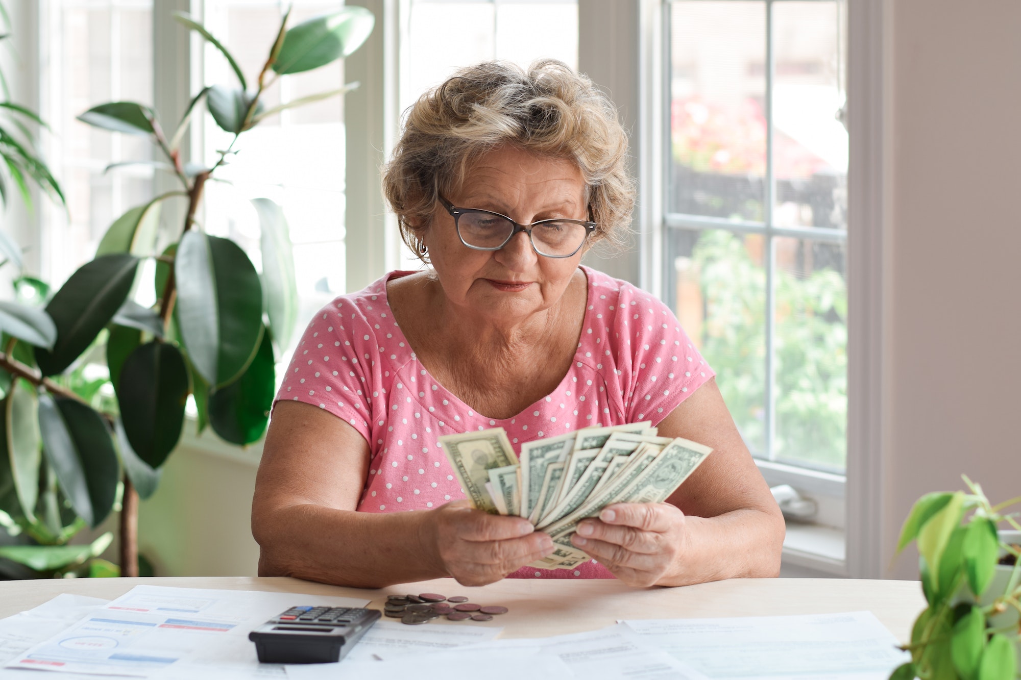Senior woman sitting at desk counting money to pay bills