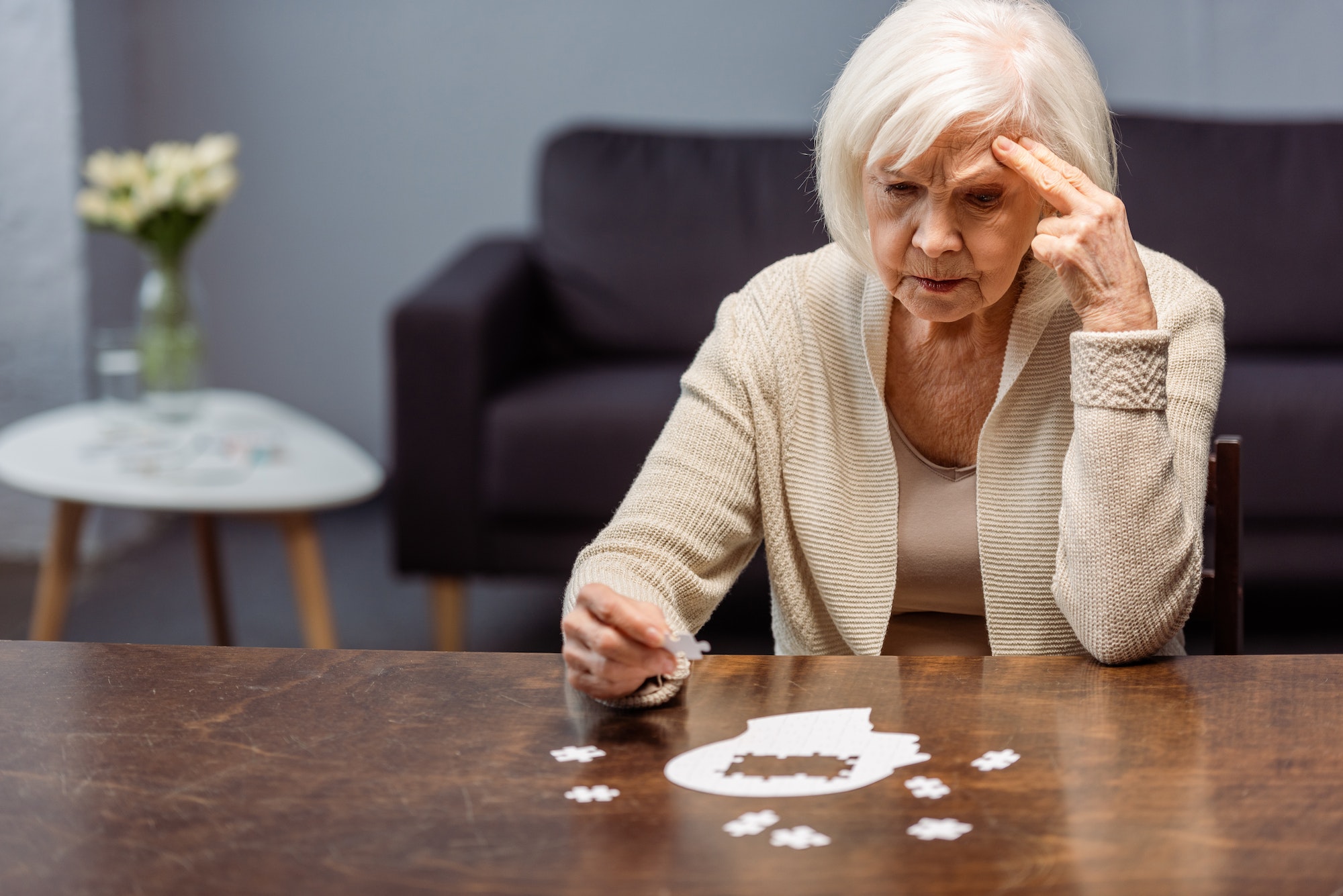 thoughtful senior woman collecting jigsaw puzzle as dementia therapy